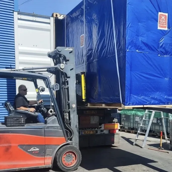 מלגזה וציוד תעשייתי ברקע של מבנה תעשייתי עם עצי דקל, שוק ישראלי